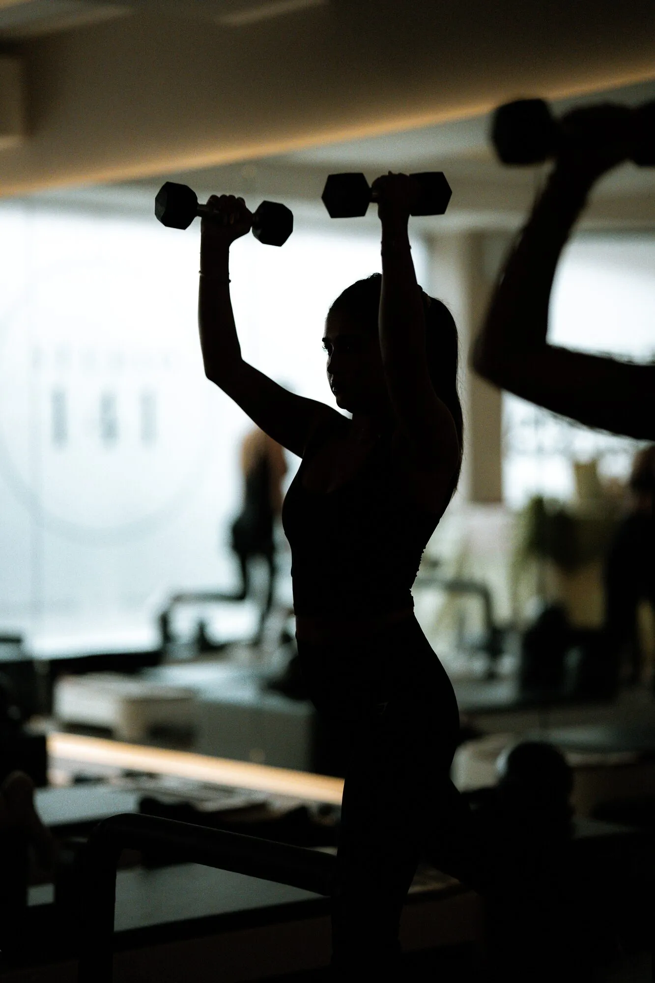 Silhouette of a member lifting dumbbells overhead beside the Studio 141 window