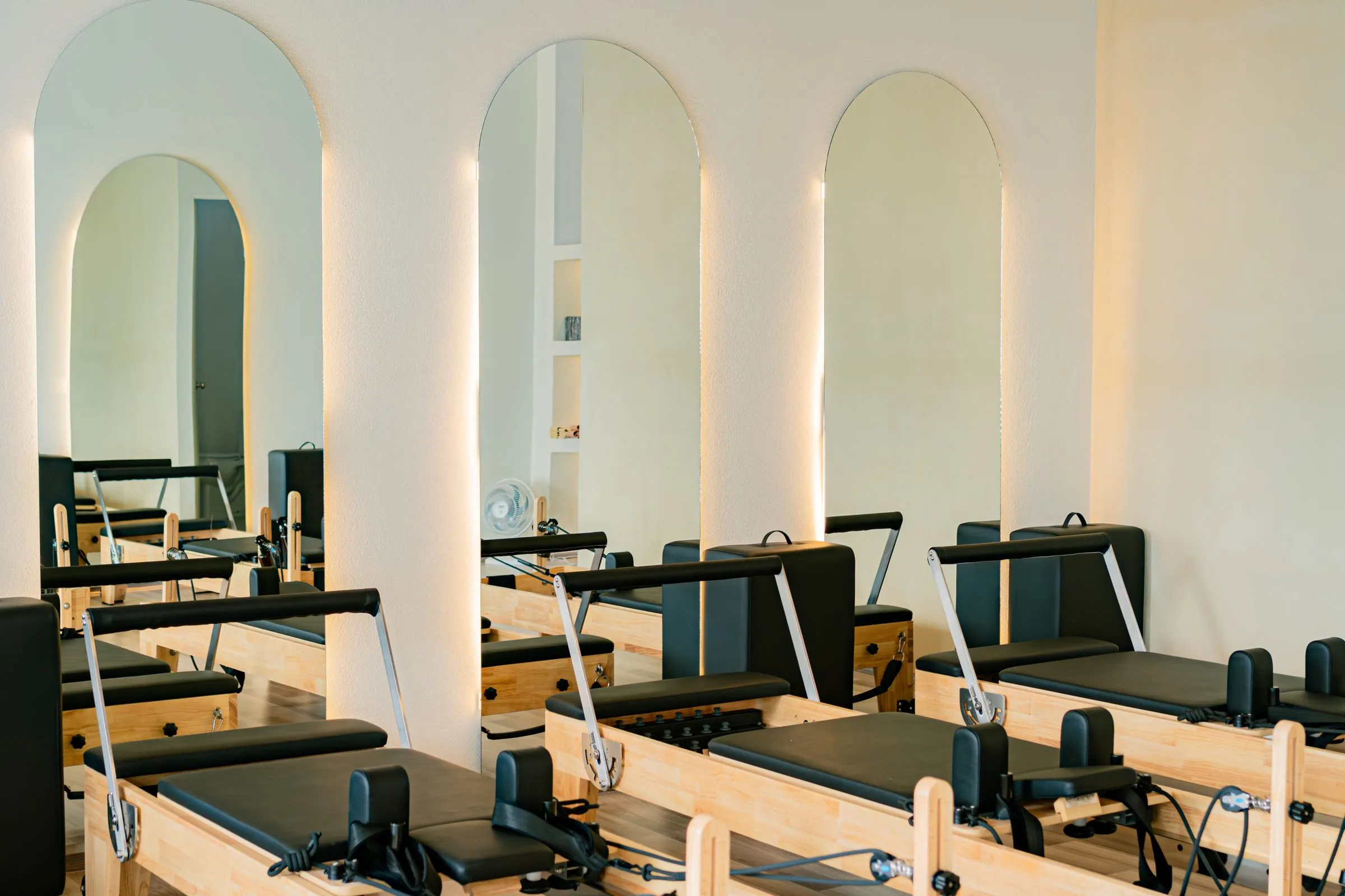 Reformer beds beneath arched, backlit mirrors in a warm studio